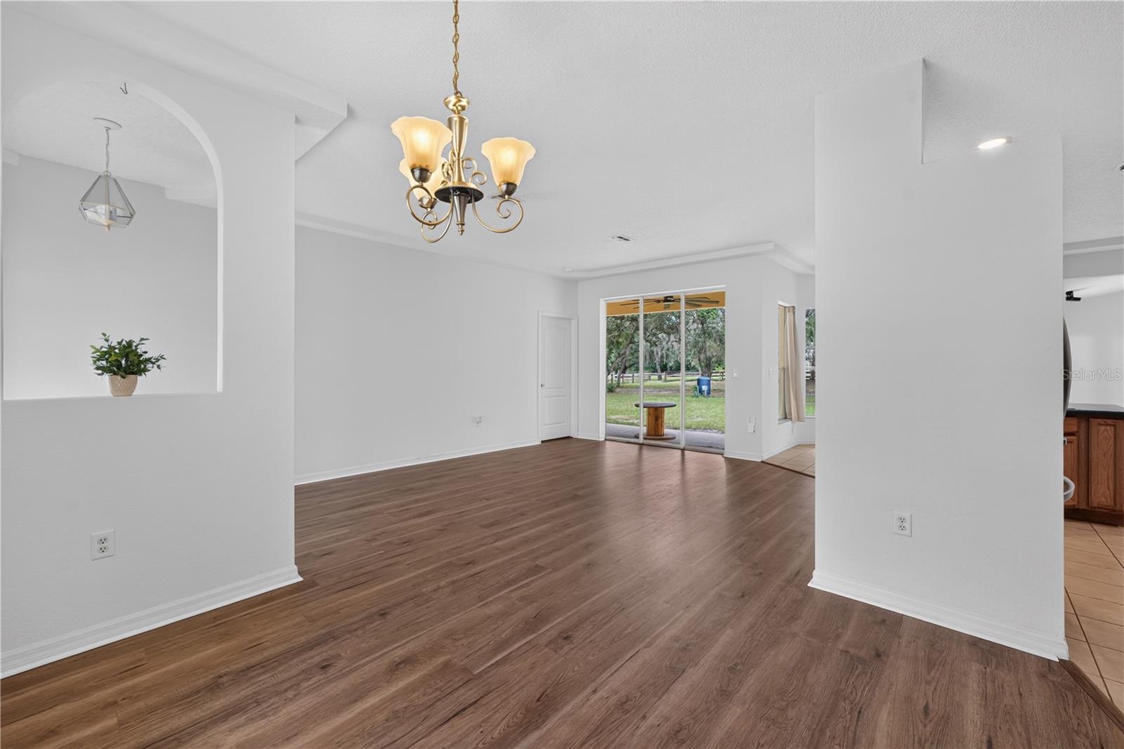 Empty living and dining area with wood-look floors, a brass chandelier, and sliding doors to the yard.