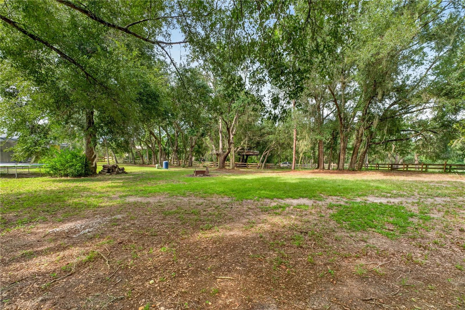 Tree-shaded yard with a wooden fence, grassy clearing, and small fire pit.