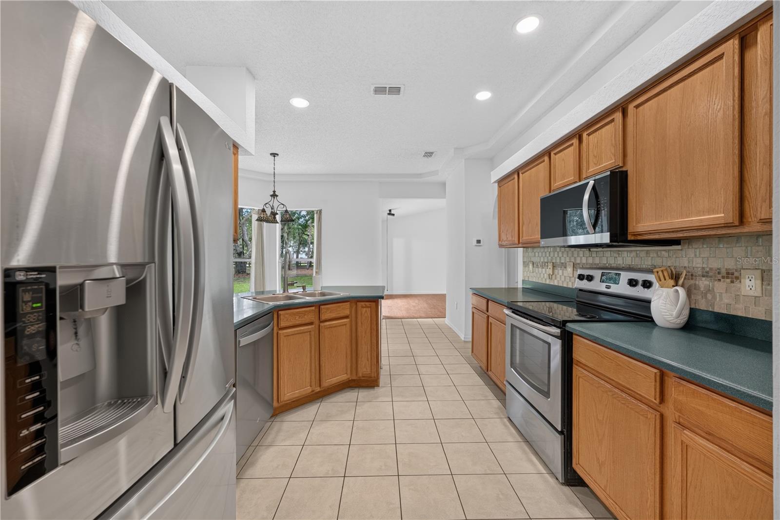 Kitchen with honey-colored cabinets, dark green counters, stainless steel appliances, and a tiled floor.