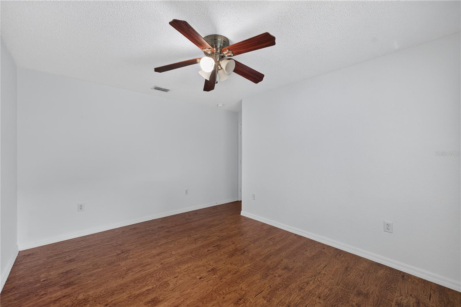 Empty room with reddish-brown wood flooring and a dark wood ceiling fan.