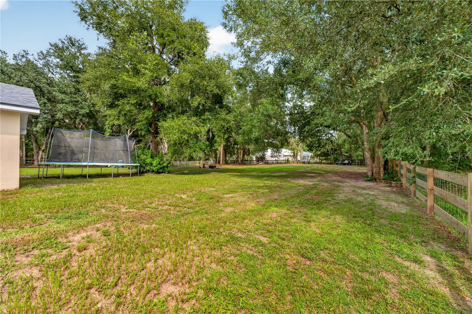 Spacious tree-shaded backyard with a trampoline and wooden fence.