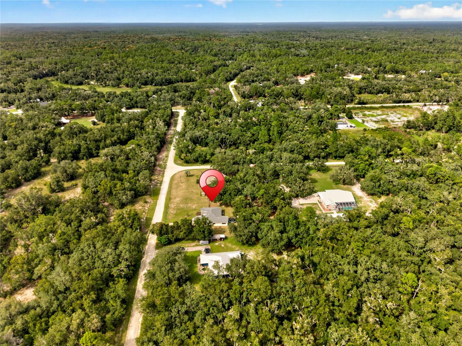 Aerial view of a home and open lot amid dense woodland, marked with a red location pin.