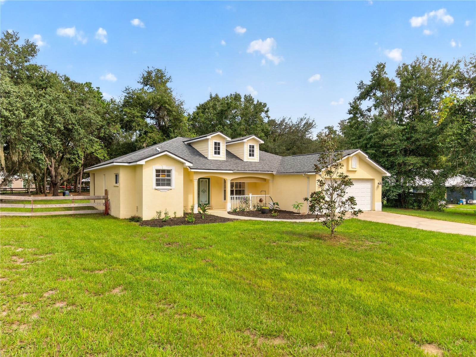 Yellow home with two roof dormers, a covered porch, attached garage, and broad green lawn.