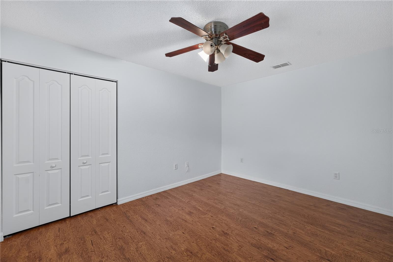 Empty bedroom with paneled closet doors, wood-look flooring, and a ceiling fan.