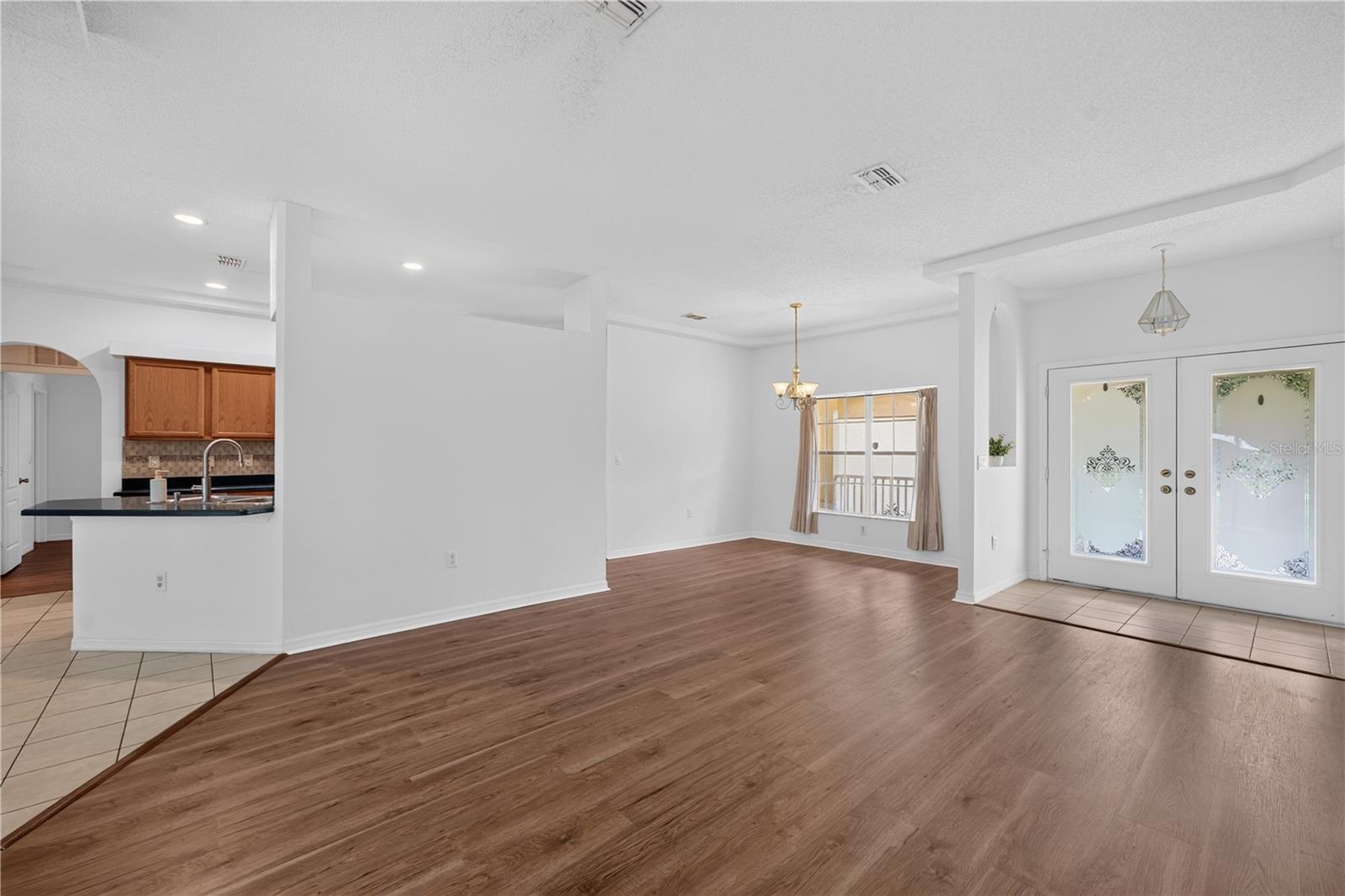 Open living and dining area with wood-look floors, a chandelier, and decorative glass entry doors.