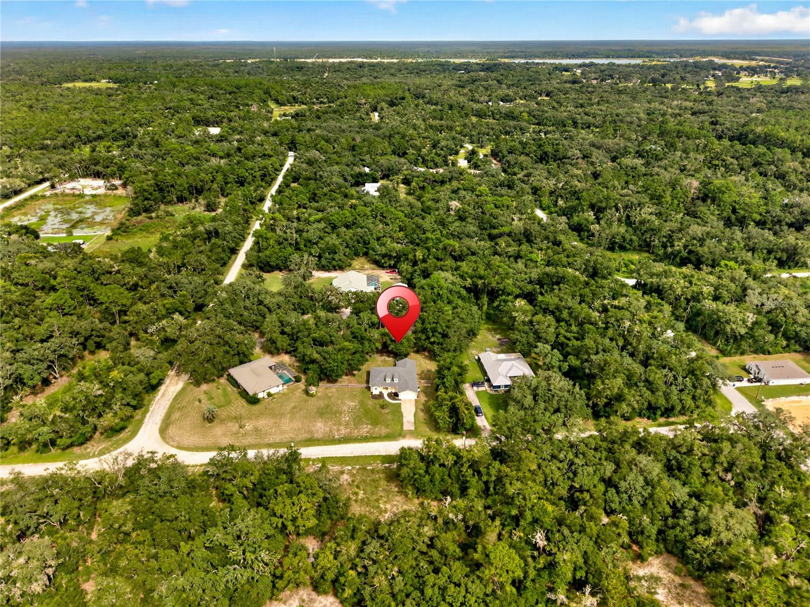 Aerial view of a wooded property marked by a red pin among scattered homes and dirt roads.