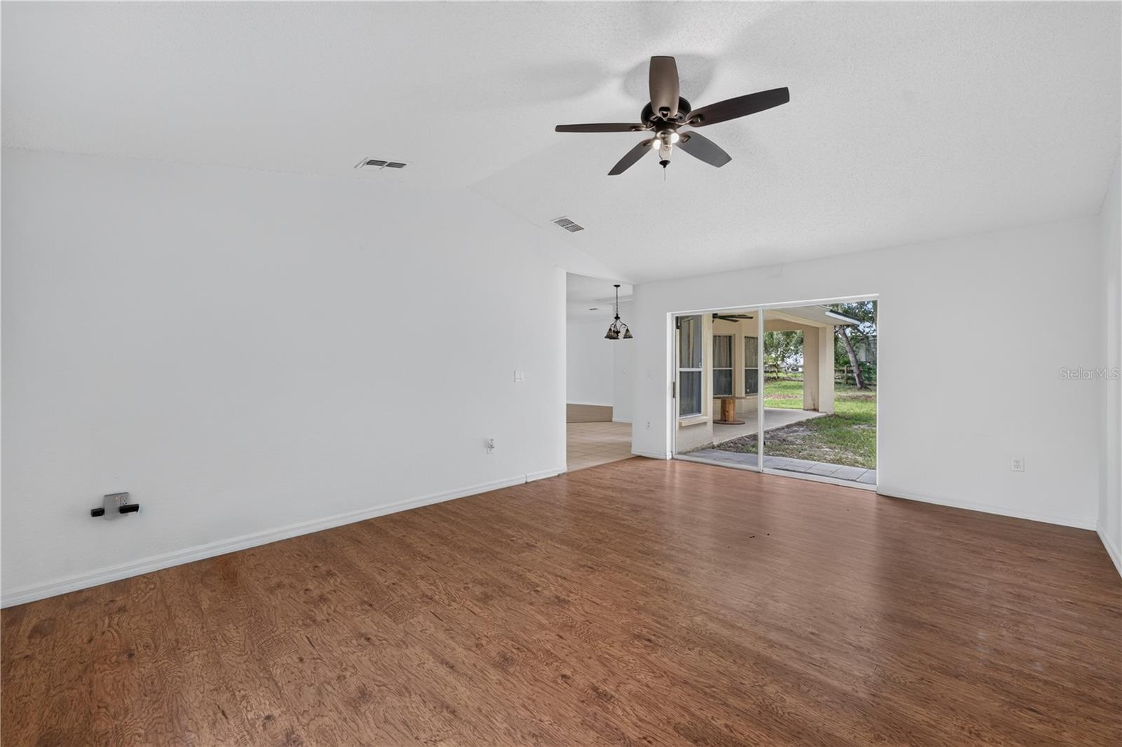 Empty living room with wood-look floors, ceiling fan, and sliding glass doors to a covered patio.