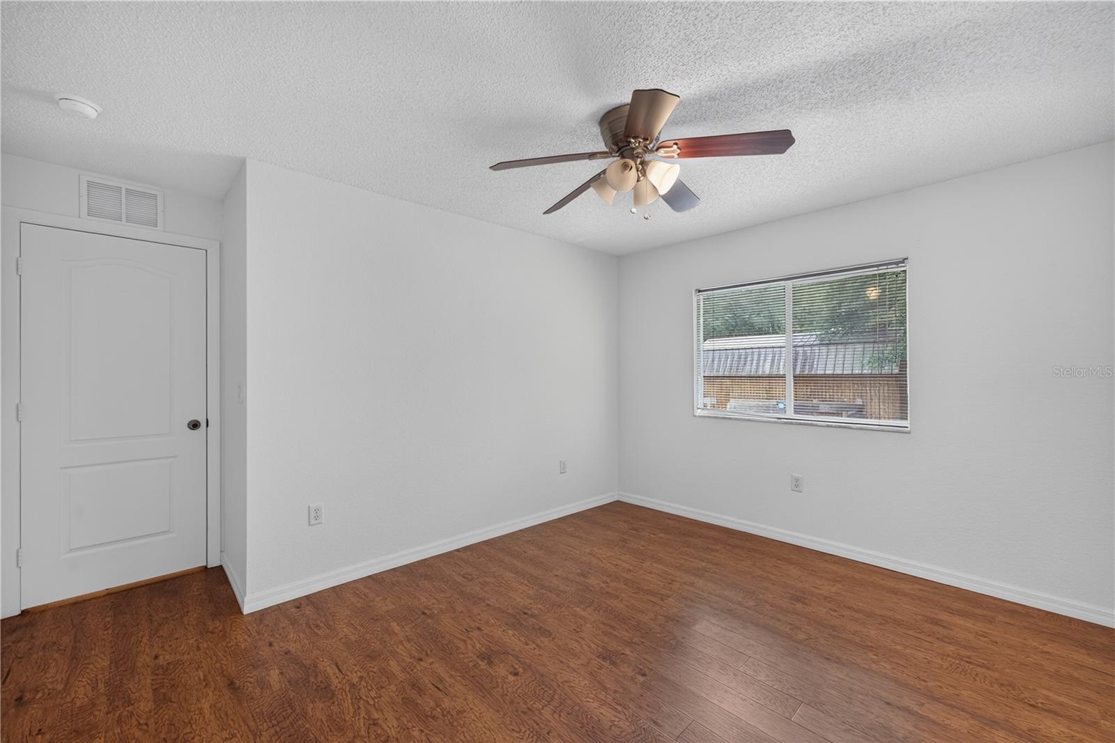 Unfurnished room with wood-look flooring, a ceiling fan, and a window with blinds.