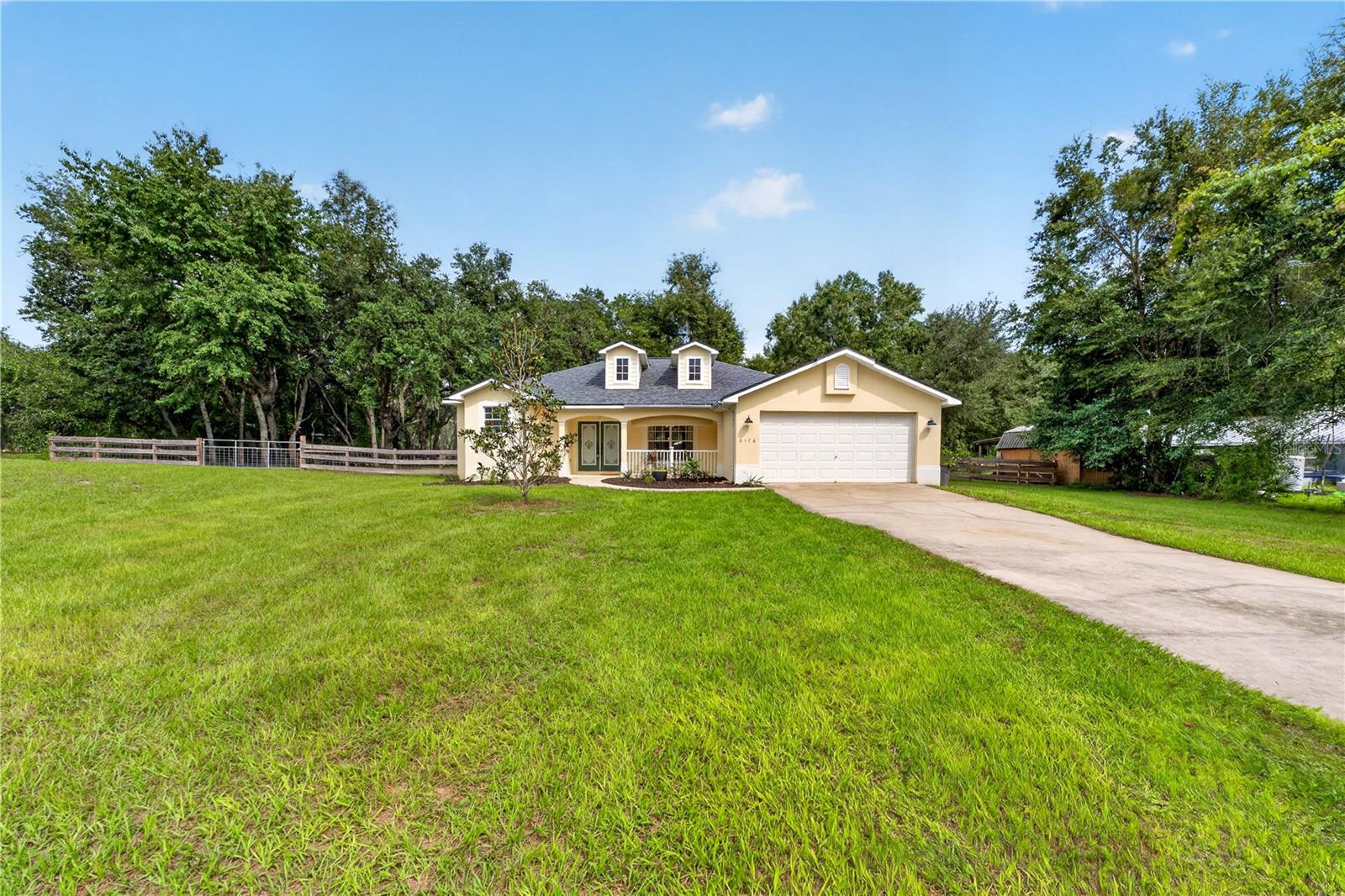 Cream-colored home with two dormers and an attached garage, set behind a broad lawn and long driveway.