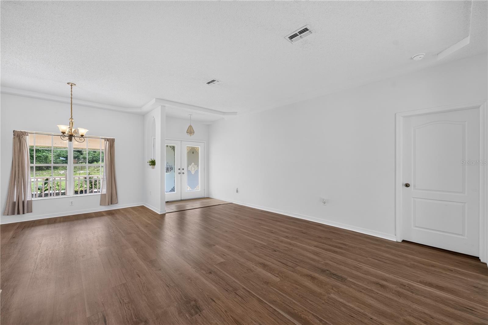 Vacant living room with wood-look flooring, a curtained window, and double glass entry doors.