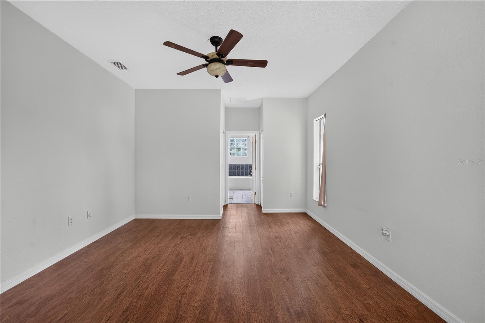 Empty room with wood-look flooring, a ceiling fan, and a doorway leading toward a tiled bathroom.
