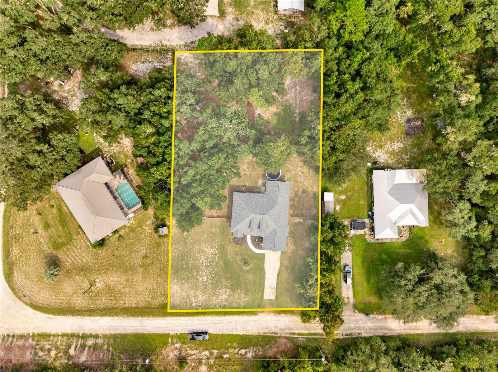 Aerial view of a wooded lot outlined in yellow, with a house and driveway near the bottom.
