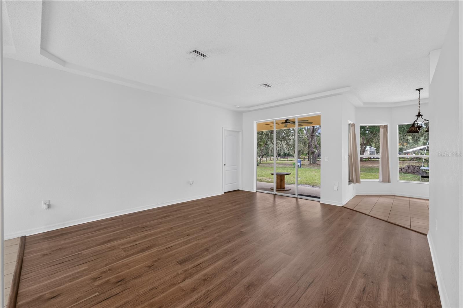 Empty living room with wood-look floors, tray ceiling, and sliding glass doors overlooking a grassy yard.