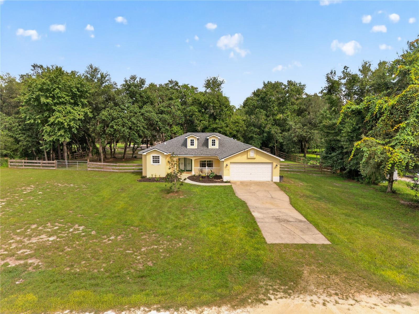 Yellow home with roof dormers and attached garage on a large grassy, tree-lined lot.