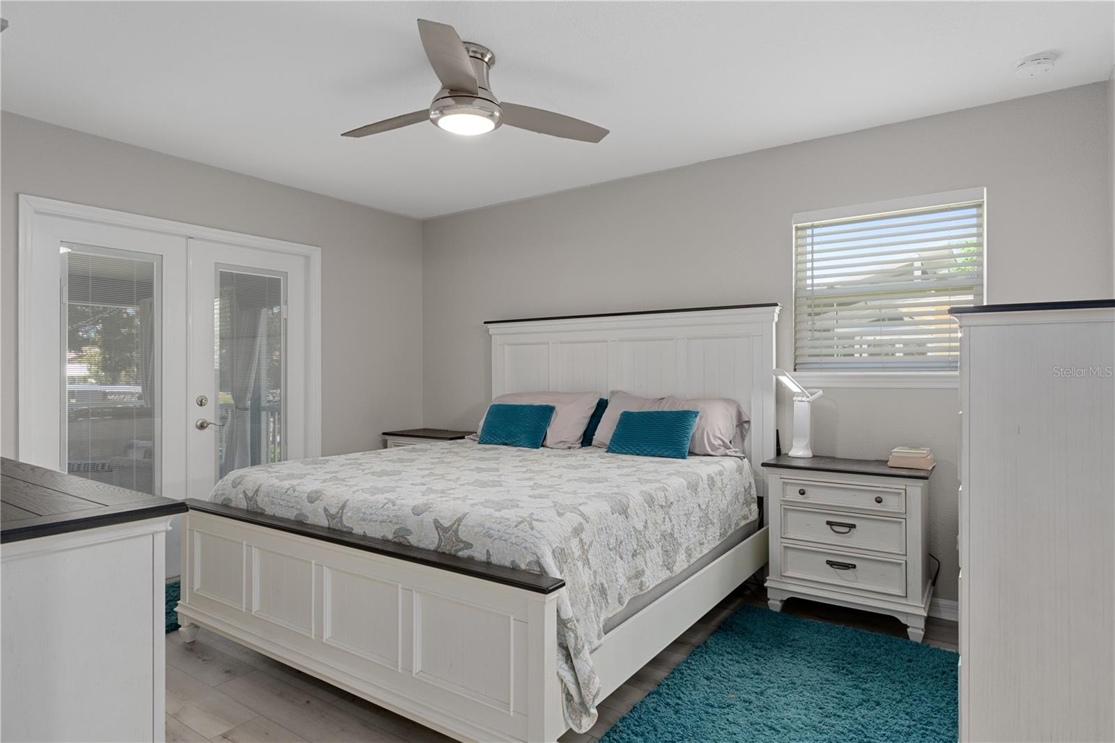 Furnished bedroom with a white paneled bed, starfish bedding, teal accents, and glass doors.
