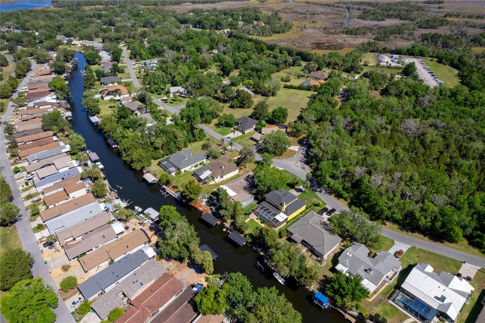 Aerial view of homes and docks along a canal beside wooded wetlands.