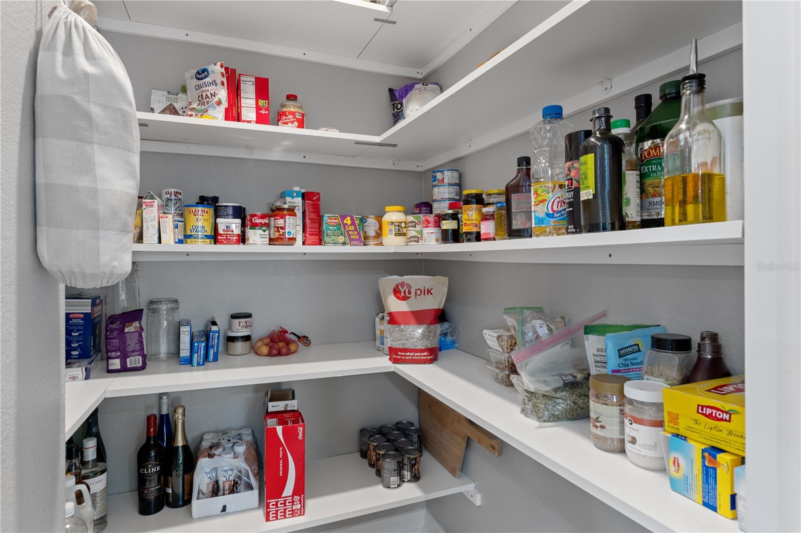 Walk-in pantry with white wraparound shelves stocked with food and cooking supplies.