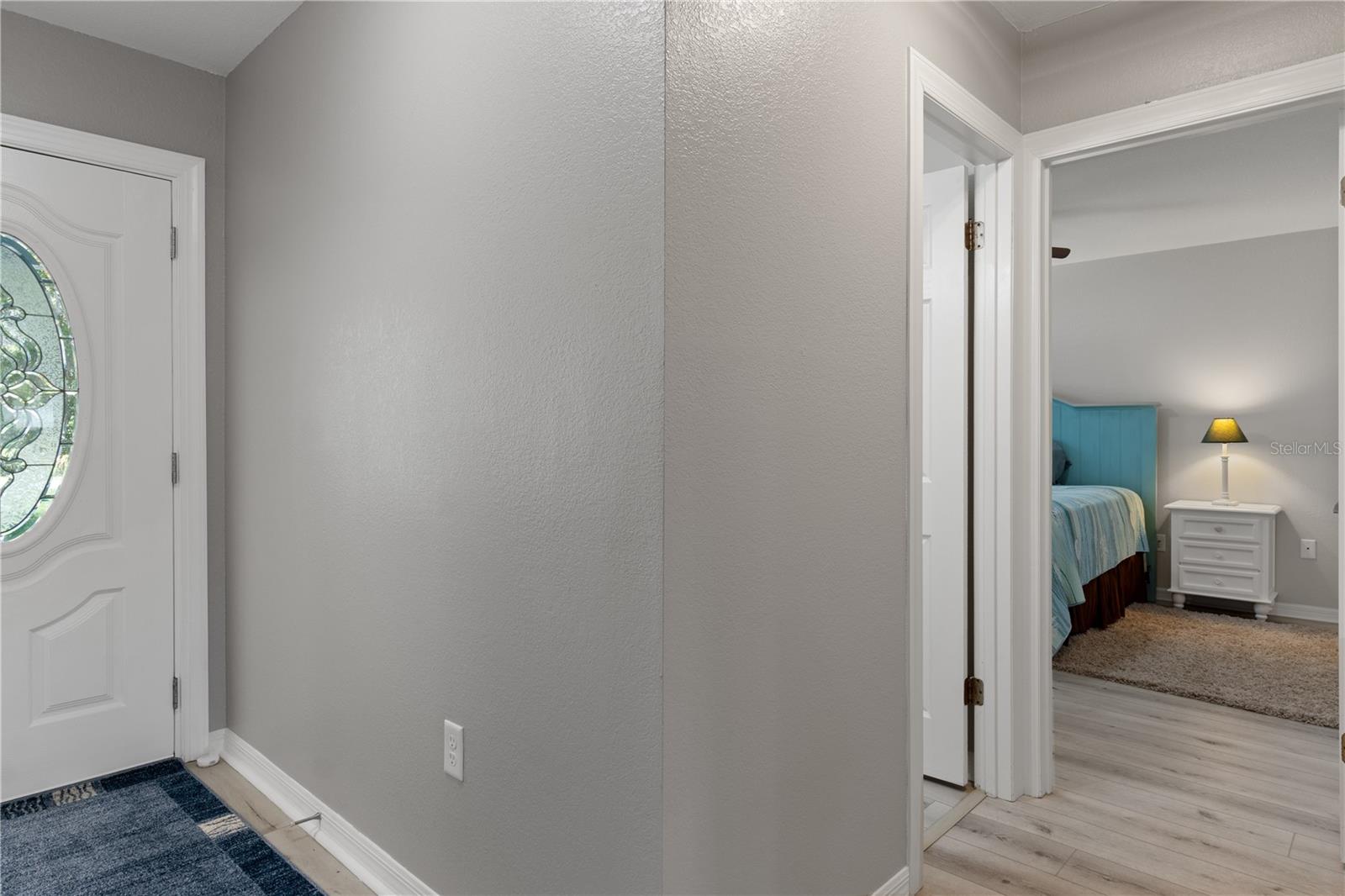 Hallway with an oval-glass front door and a view into a bedroom with a blue bed.