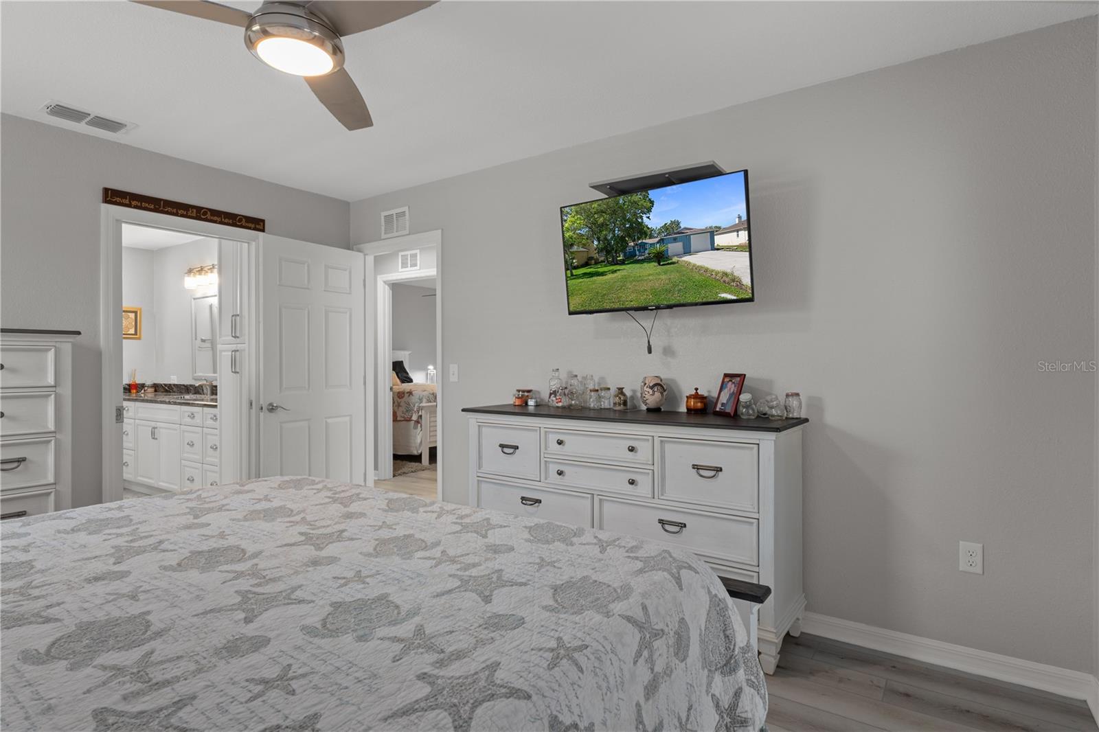 Bedroom with starfish-patterned bedding, ceiling fan, wall-mounted television, and white dresser.