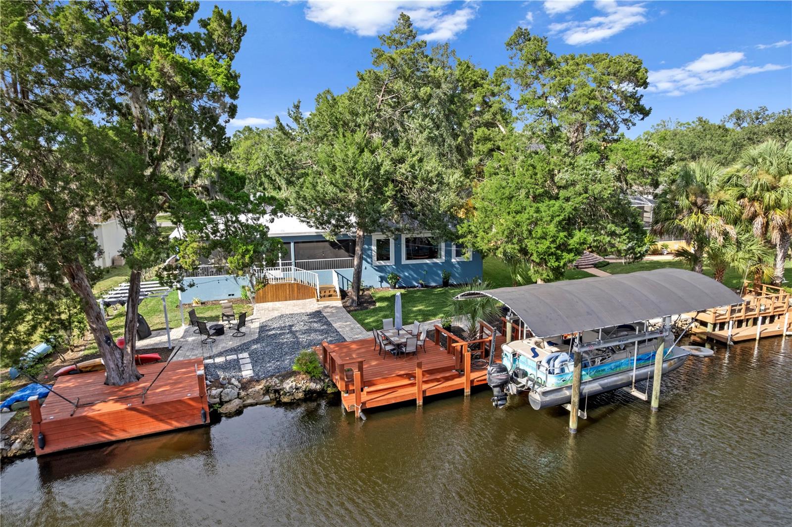 Waterfront home with wooden docks, a covered boat lift, and a pontoon boat on the canal.