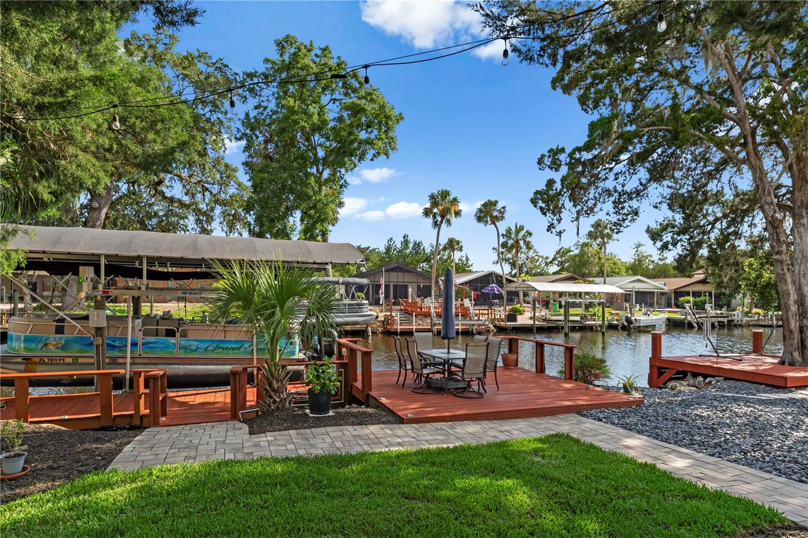 Waterfront dock and patio beside a canal, with boats under covered lifts across the water.