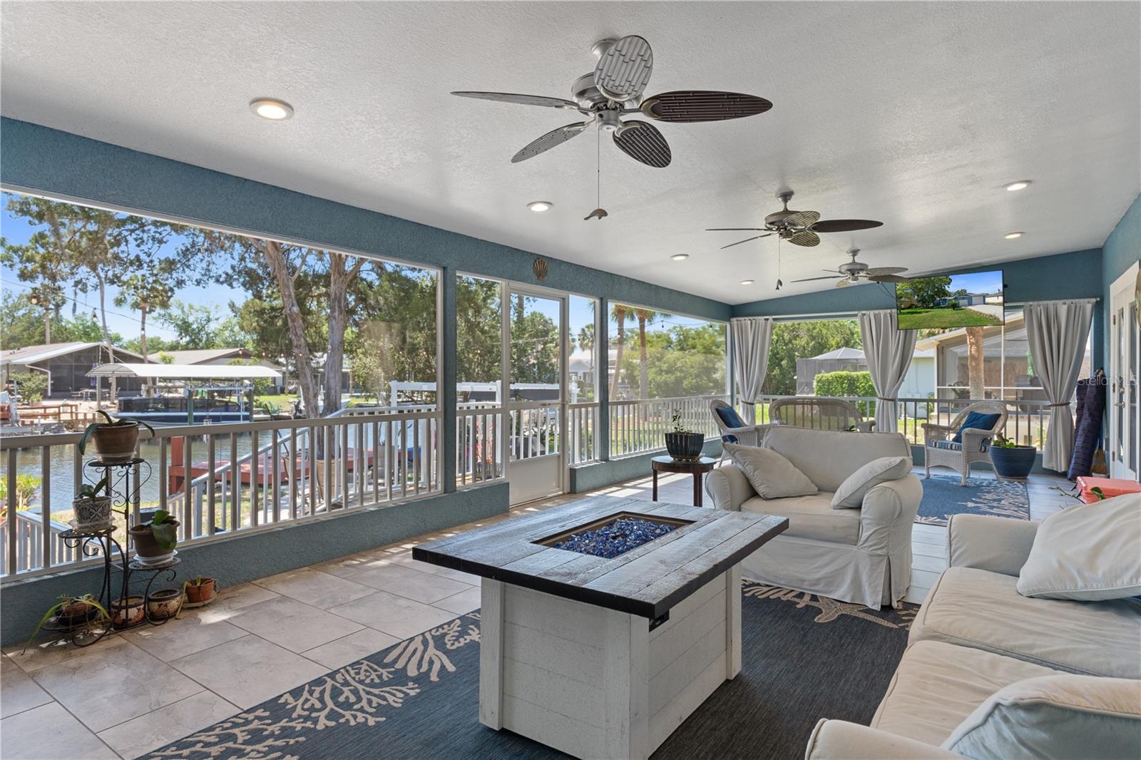 Furnished sunroom with a square fire table and broad windows overlooking a canal.