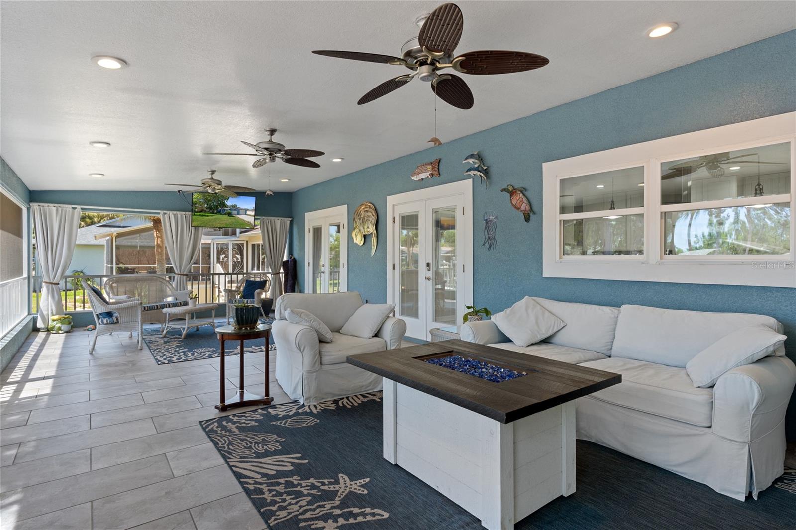 Enclosed sunroom with white sofas, blue walls, ceiling fans, and windows overlooking the yard.