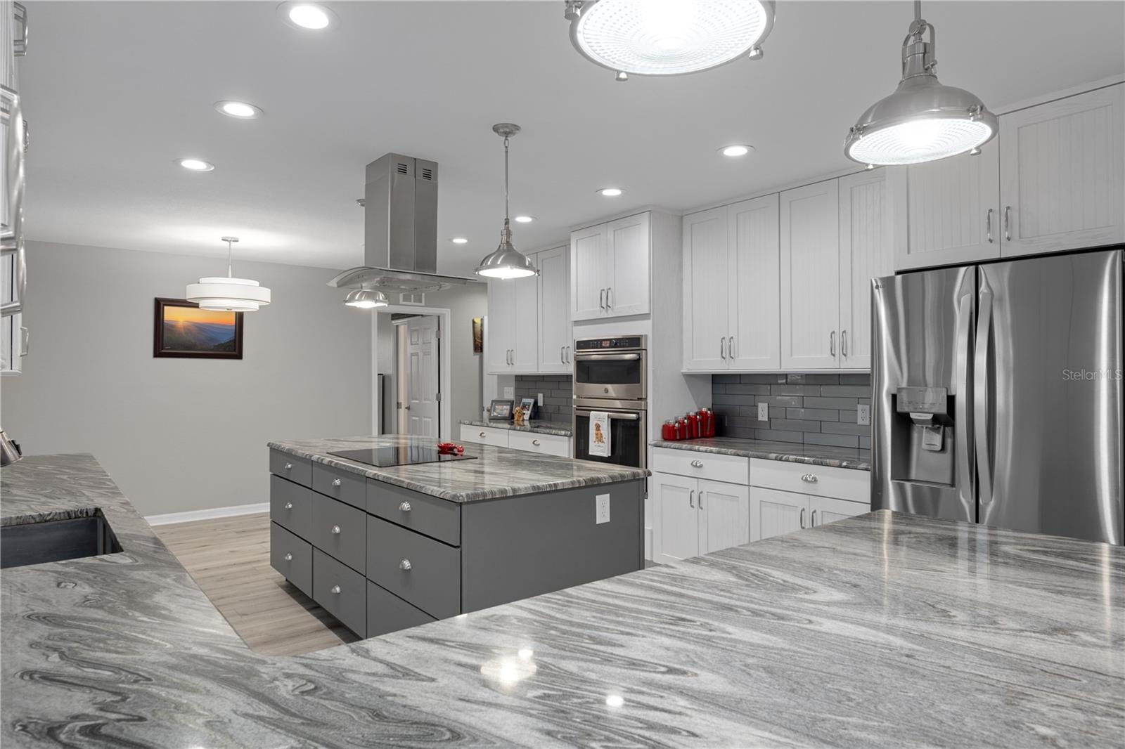 Kitchen with a large gray island, veined stone countertops, white cabinets, and stainless steel appliances.