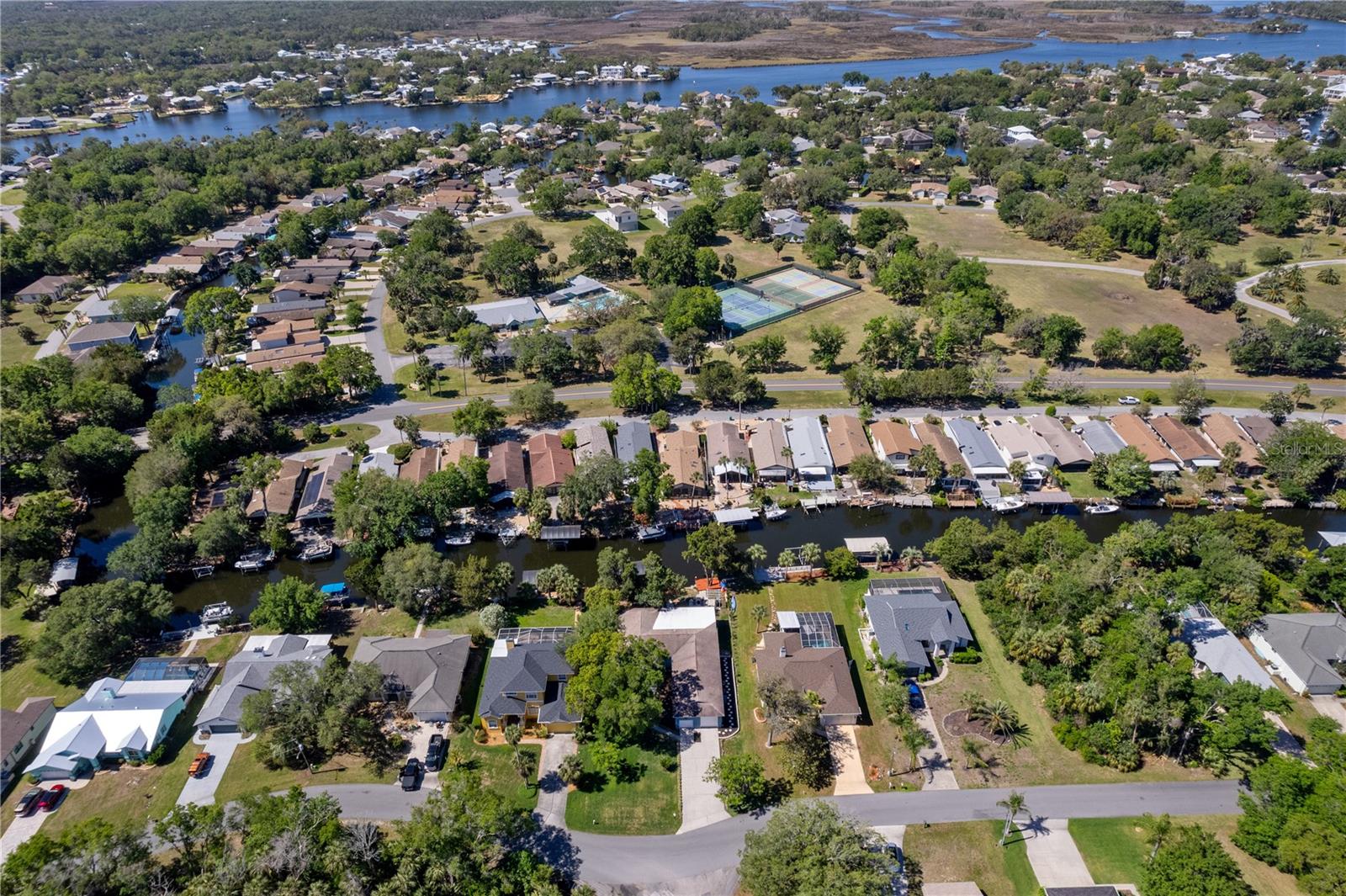 Aerial view of canal-side homes and docks, with waterways and tennis courts in the neighborhood.