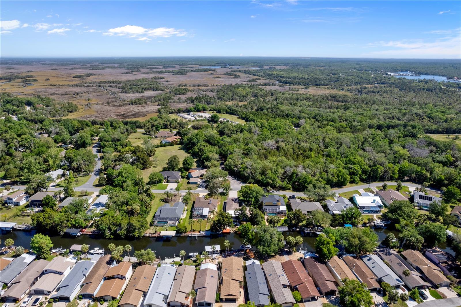 Aerial view of canal-front homes beside expansive wooded wetlands.