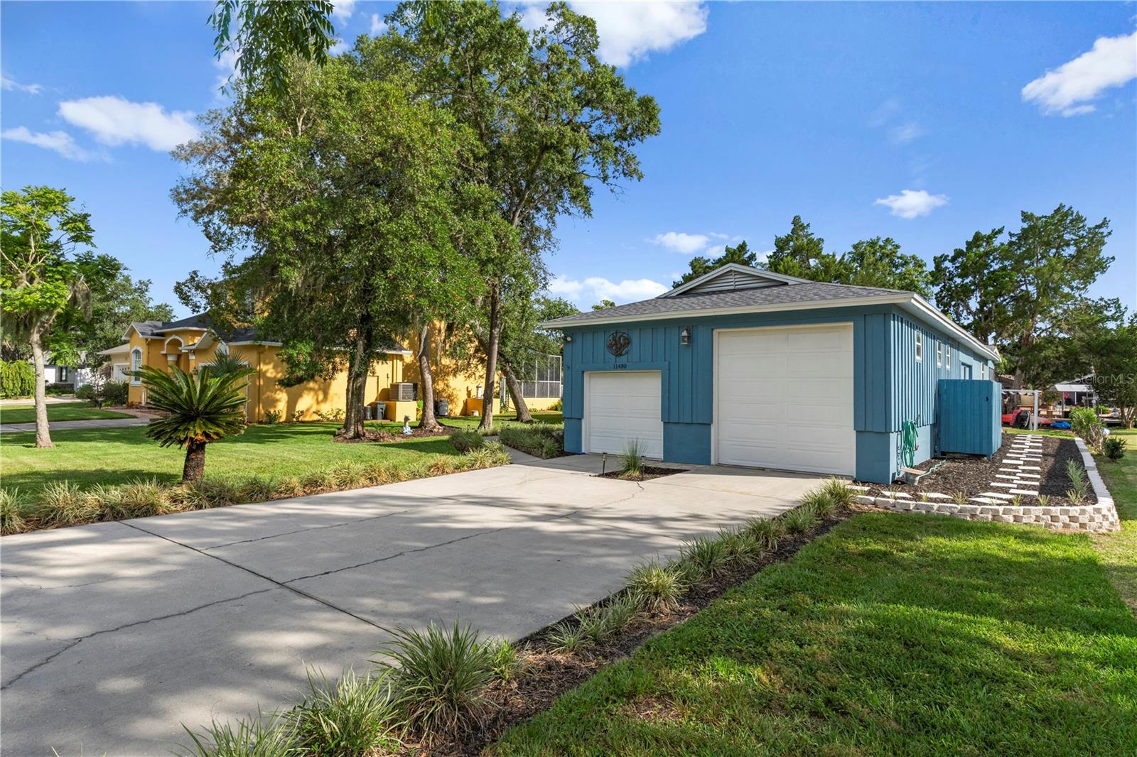 Blue detached garage with two white doors beside a wide concrete driveway.