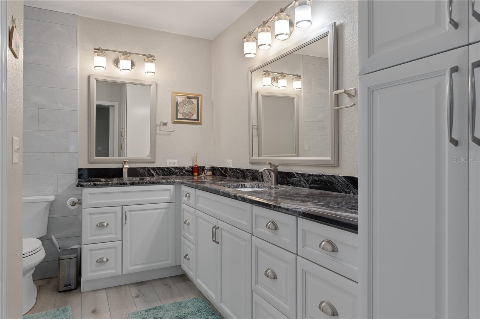 Bathroom vanity with black stone countertops, white cabinetry, two sinks, and framed mirrors.
