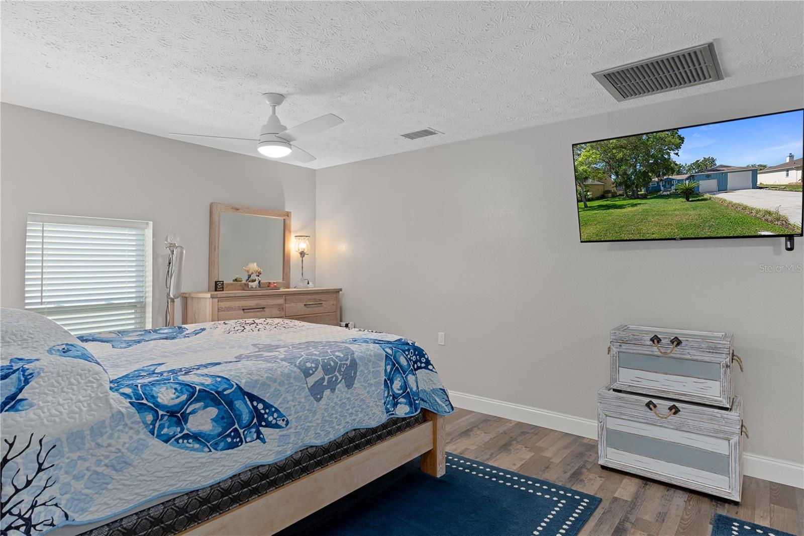 Bedroom with a blue sea-life quilt, wood dresser and mirror, and wall-mounted television.
