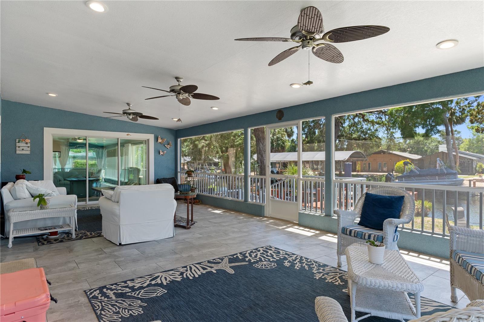 Enclosed lanai with wicker seating and large windows overlooking a canal and docked boats.