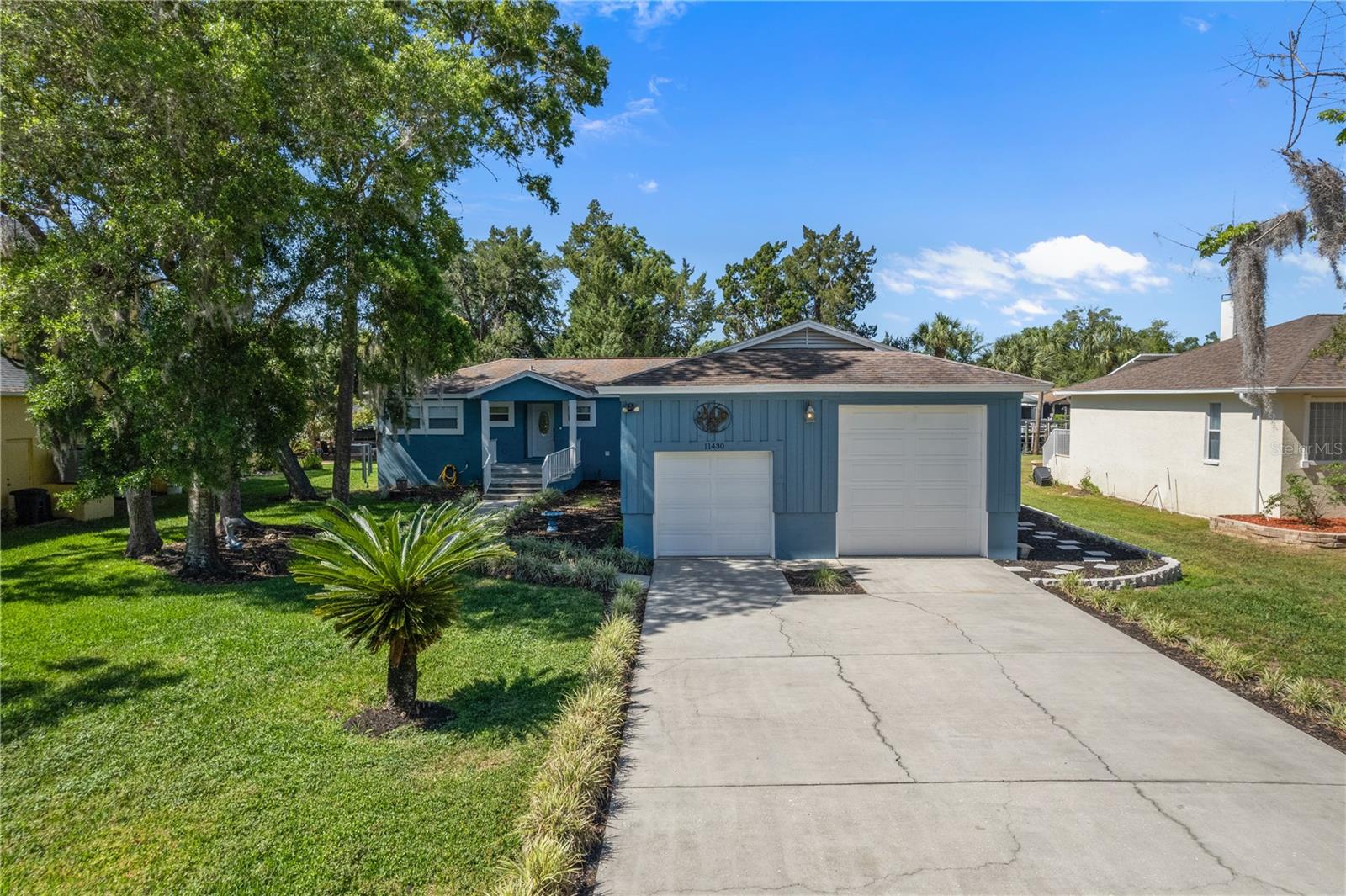 Blue single-story home with two garage doors, a wide driveway, and mature trees.