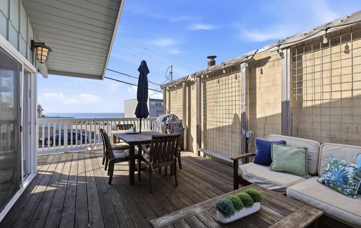 Furnished ocean-view deck with outdoor dining table, umbrella, and cushioned seating.