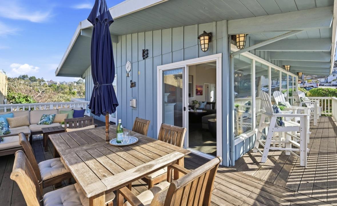 Furnished wooden deck patio with outdoor dining table, cushioned seating, and a covered glass porch.