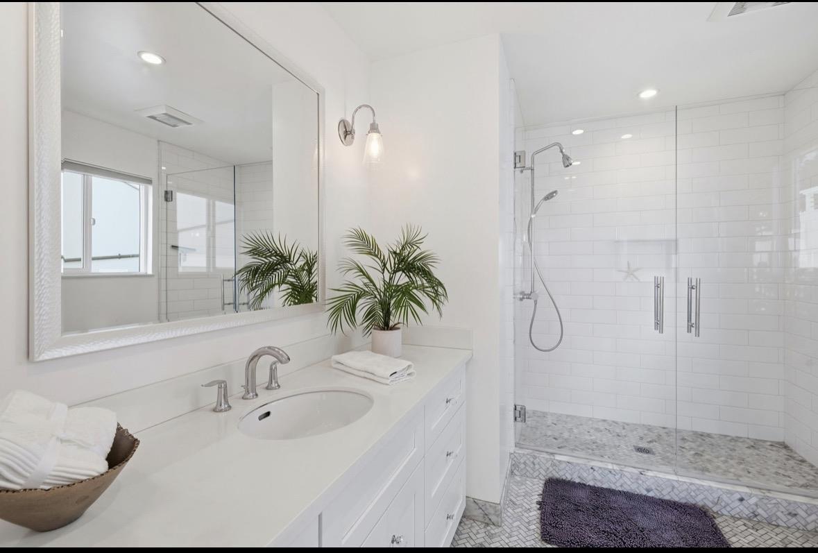 Bright bathroom with a white vanity, large mirror, and glass-enclosed subway-tile shower.