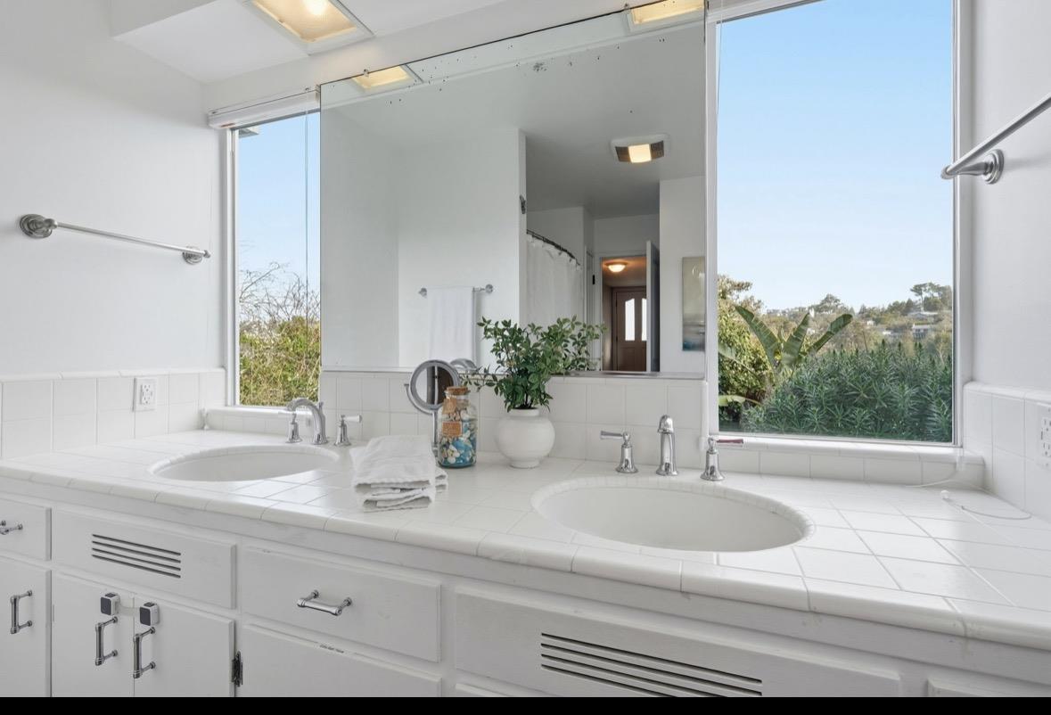 Bathroom with a double-sink white tiled vanity and a wide window overlooking greenery.