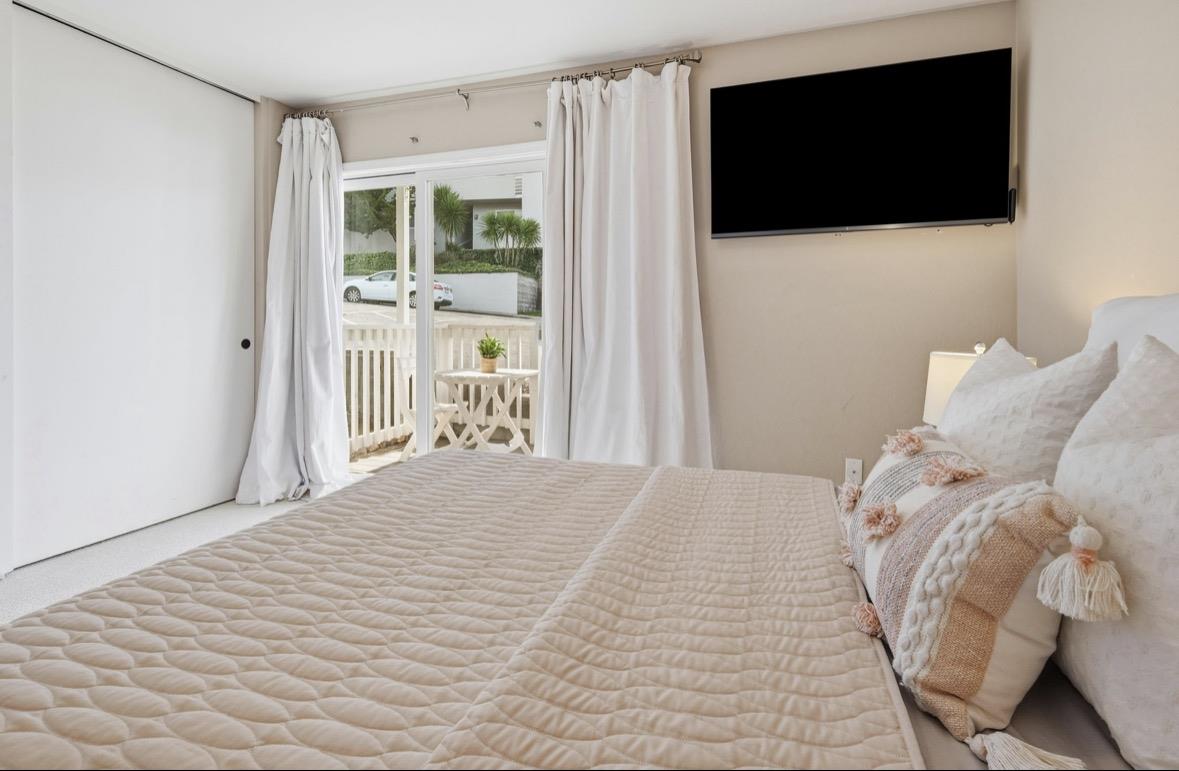 Bedroom with a quilted bed, wall-mounted television, and sliding doors to a small balcony.