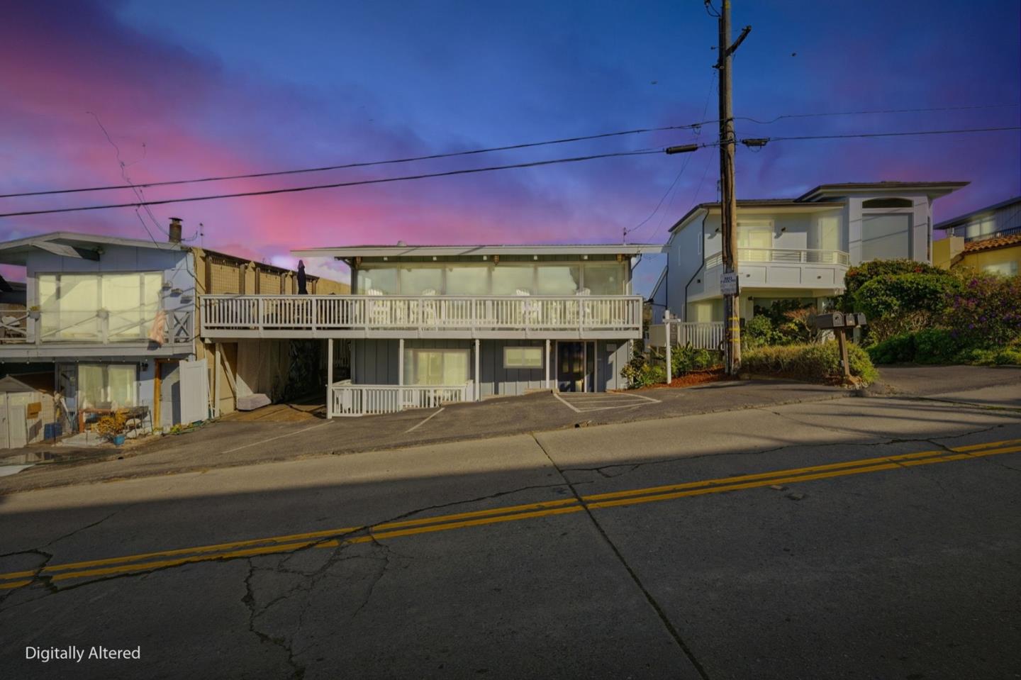 Two-story gray home with a wide elevated deck and white railings at dusk.