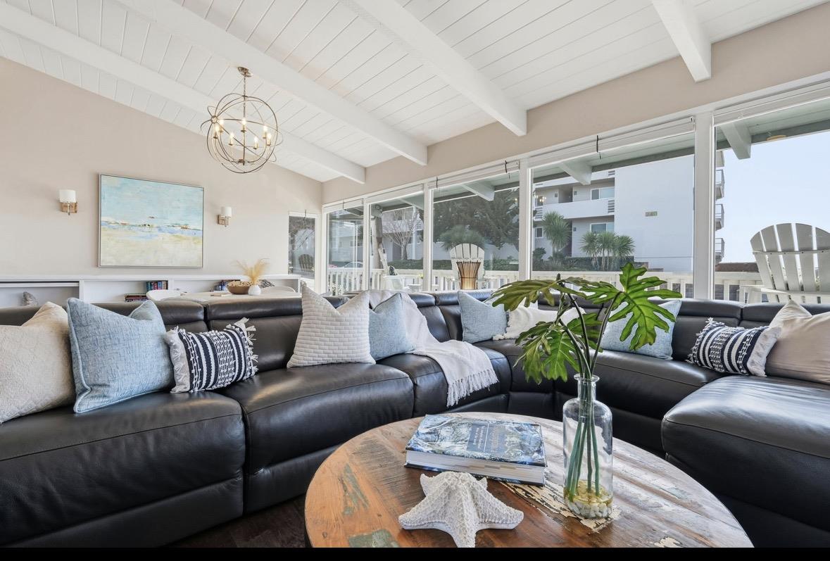Living room with a black leather sectional, vaulted white ceiling, and wide windows facing a deck.