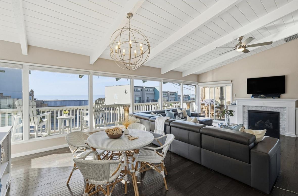 Living and dining room with a vaulted ceiling, fireplace, and ocean views through large windows.