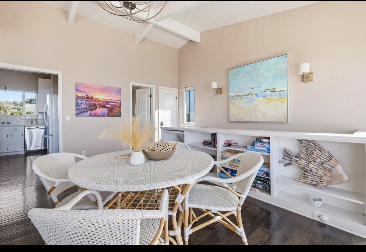 Dining area with a white wicker table, built-in shelves, and coastal artwork.