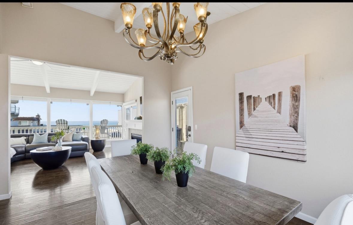 Dining room with a rustic wood table and chandelier, opening to an ocean-view living area.