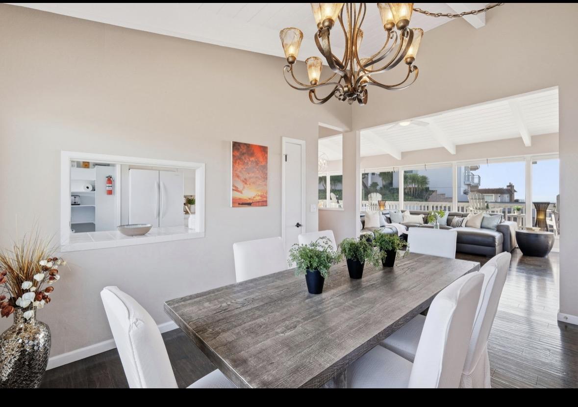 Dining room with a long gray wood table, white chairs, and an adjoining living area opening onto a deck.