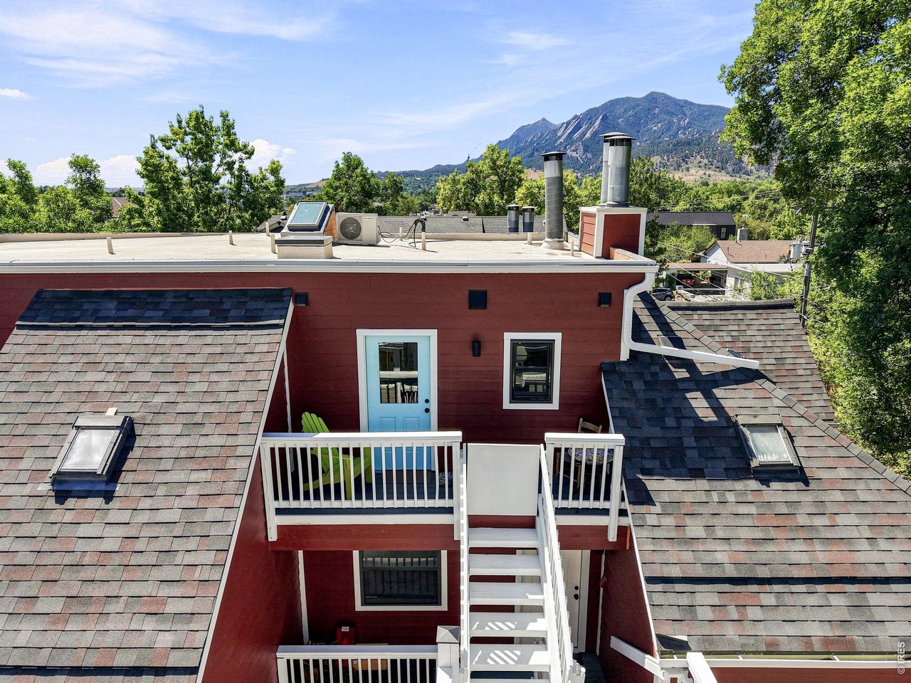 Red home with white balconies and exterior stairs, backed by a mountain view.