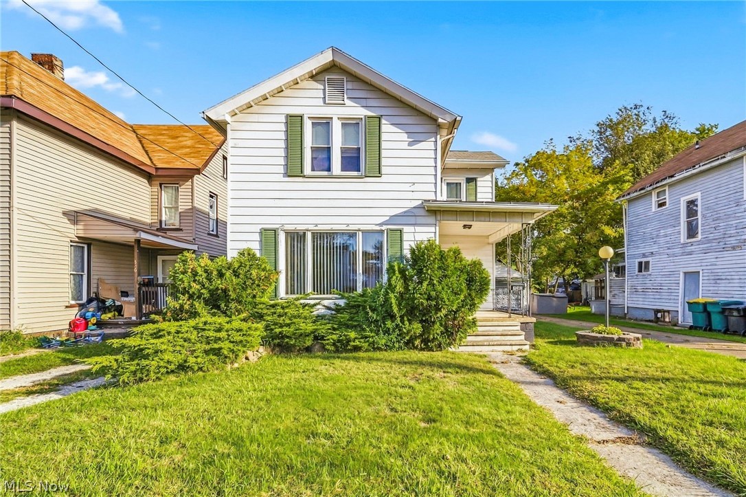 White two-story house with green shutters, a covered patio, and grassy yard.