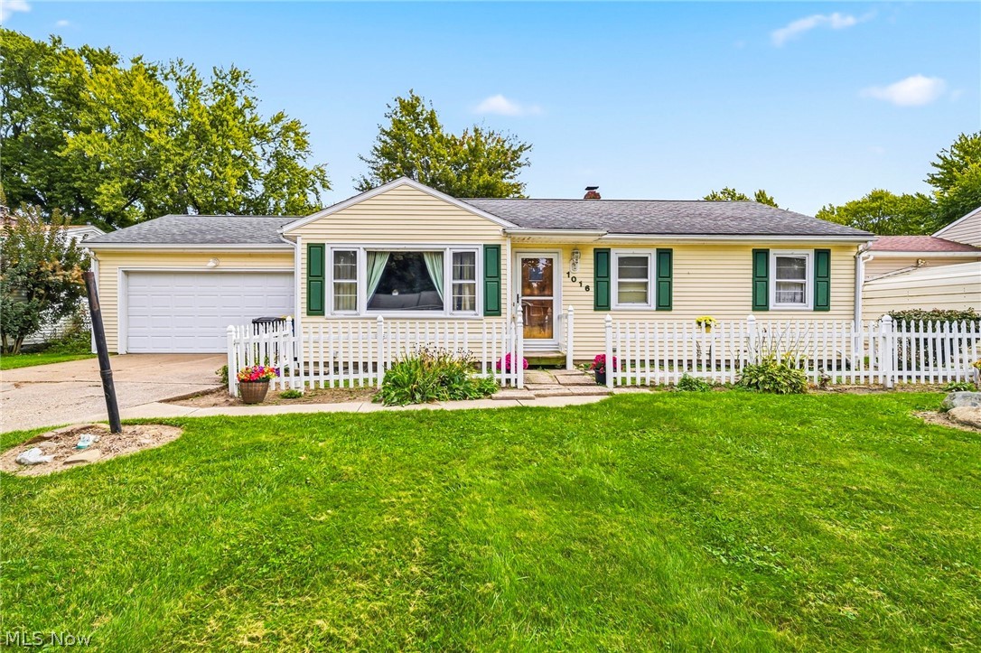 Single-story cream home with green shutters, attached garage, and white picket fence.