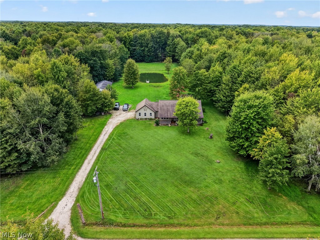 House on a wooded property with a broad lawn, gravel driveway, and small pond.